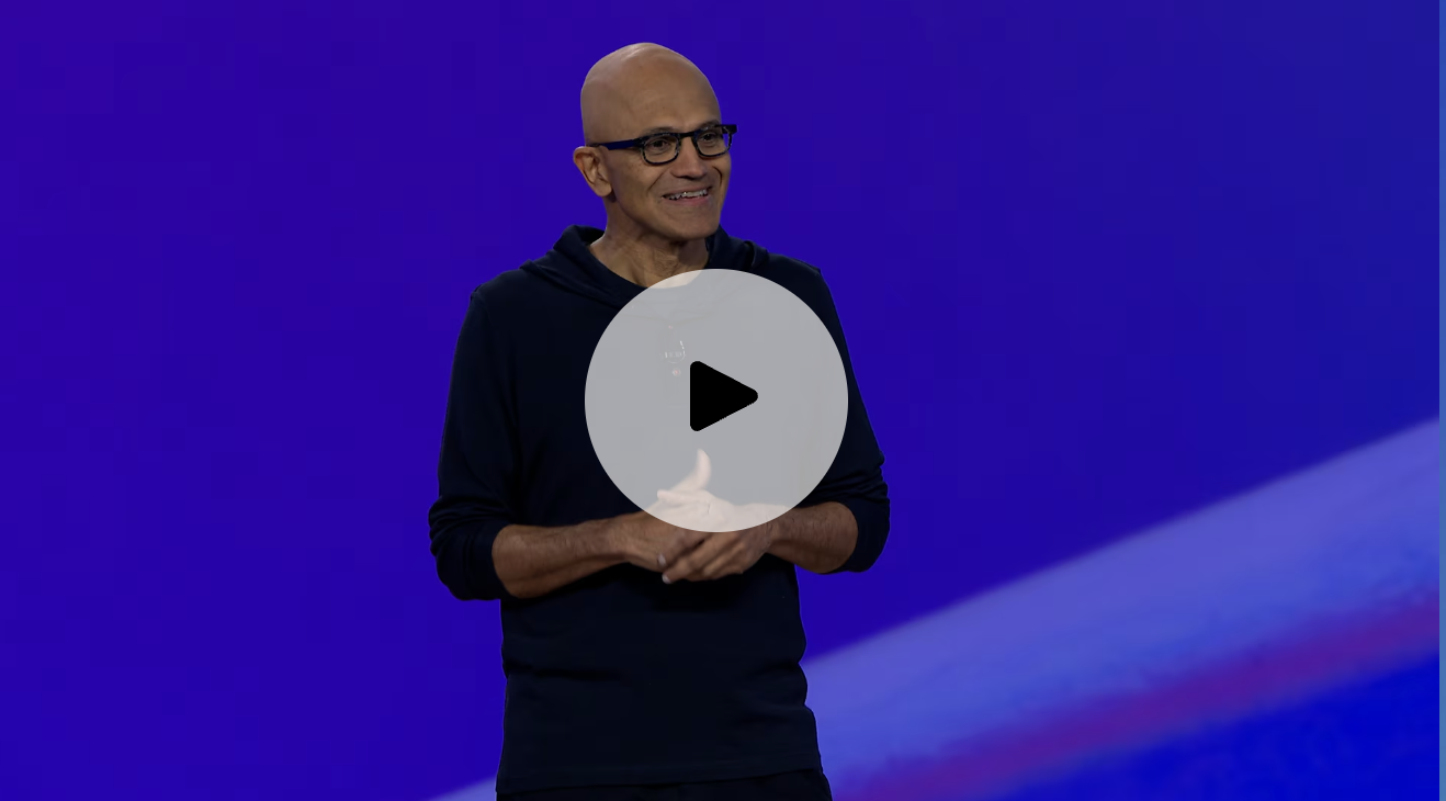 Microsoft CEO, Satya Nadella, stands in front of a blue background. There is a click to play button at the center of the image.